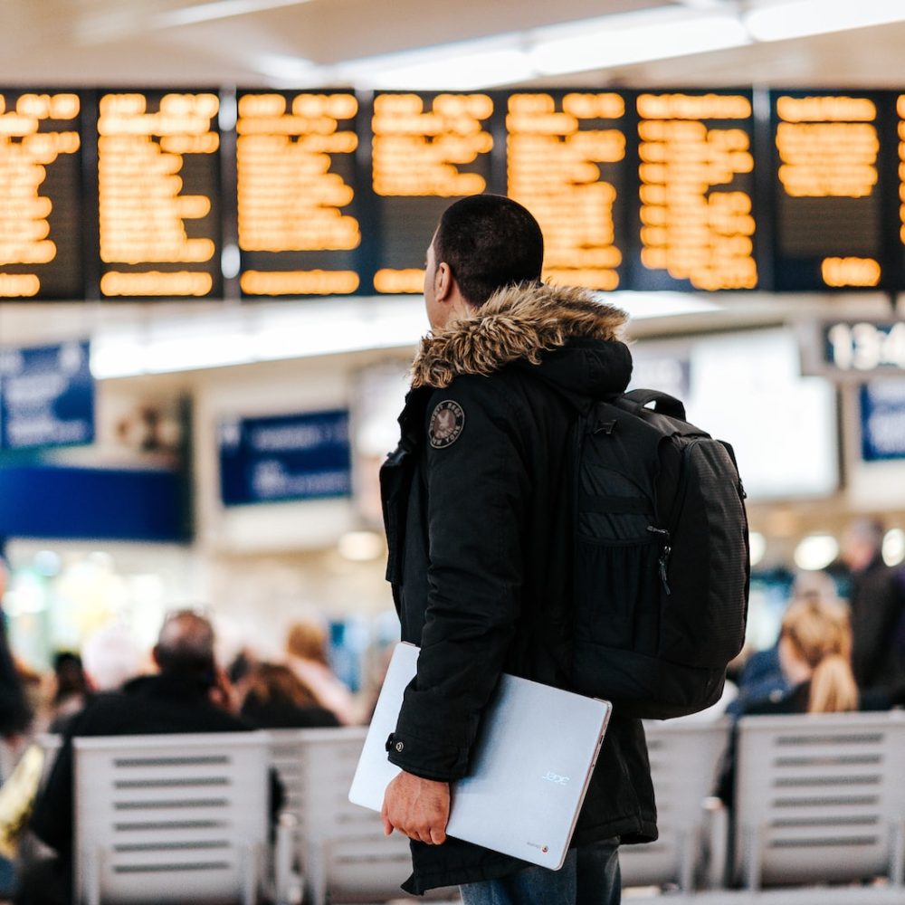 man standing inside airport looking at LED flight schedule bulletin board